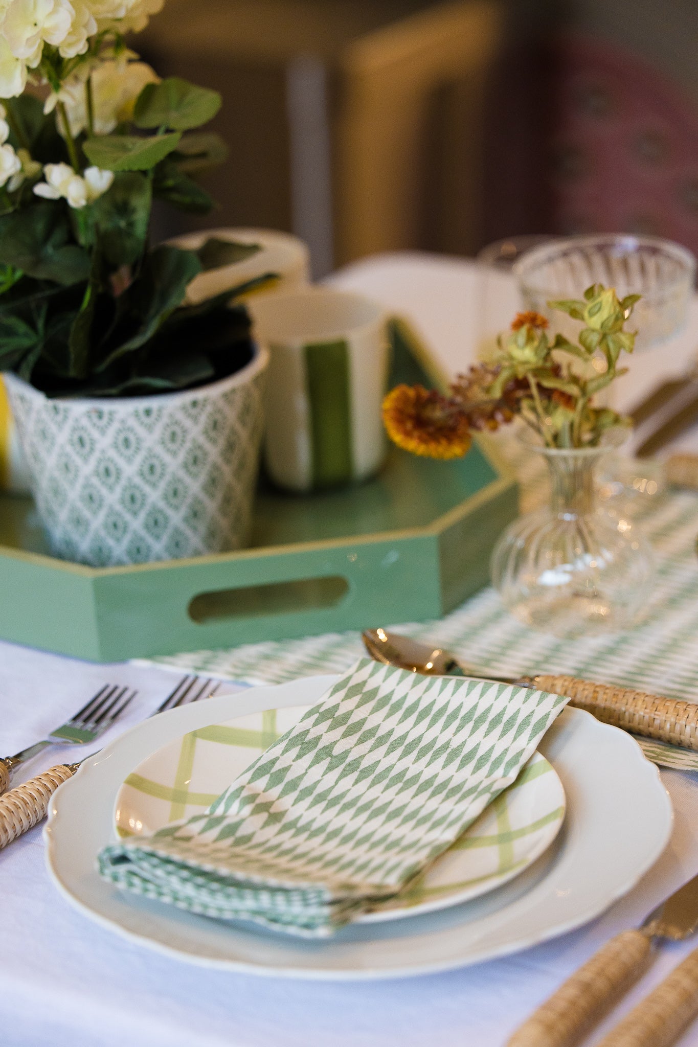 Spring table setting with green and white decor, including plates, napkins, and a vase with flower on a green lacquered tray