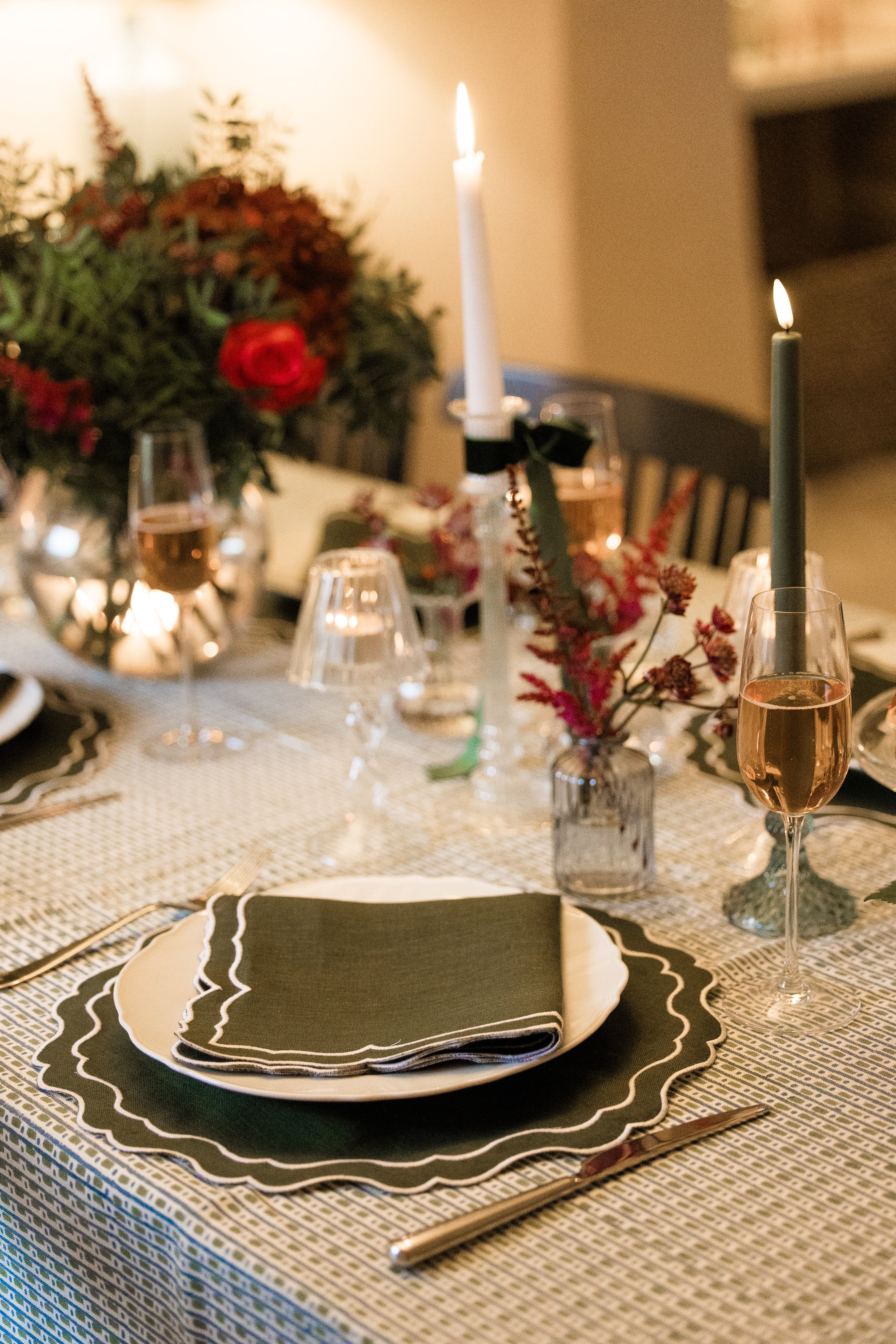 Elegant dinner table setting with tall glass candlesticks, flowers, and fern green block printed table linens.