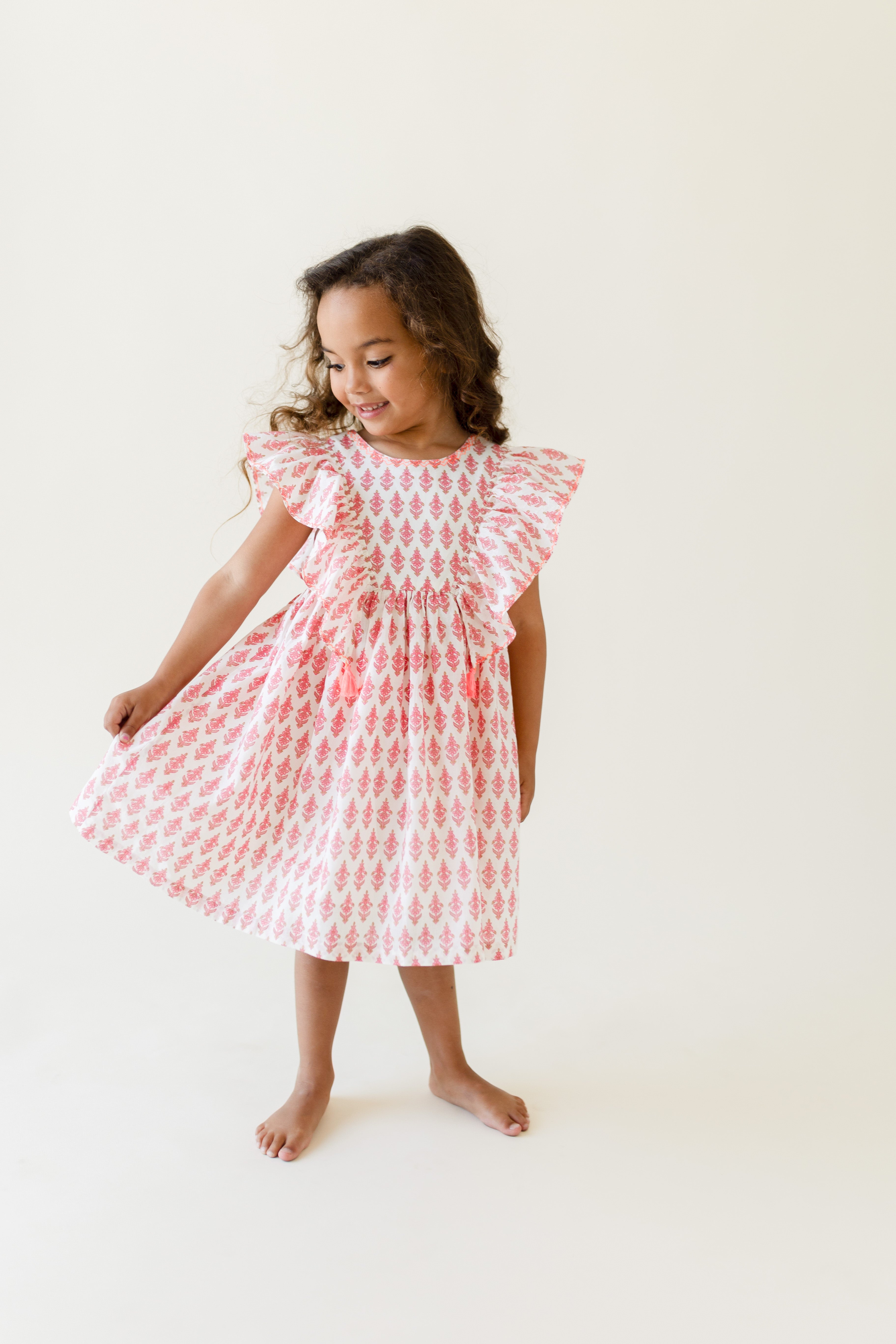 A girl wearing a short-sleeved pink dress with a daisy print design.